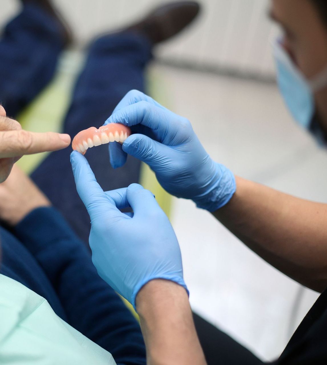 A person wearing blue gloves is holding a denture