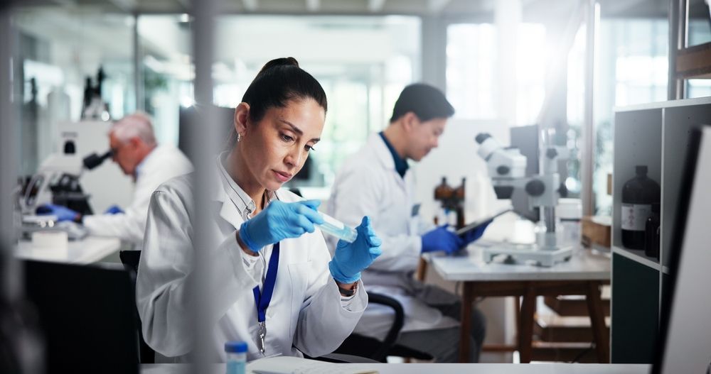 Scientists in a lab examining a sample with pipettes and gloves at workstations
