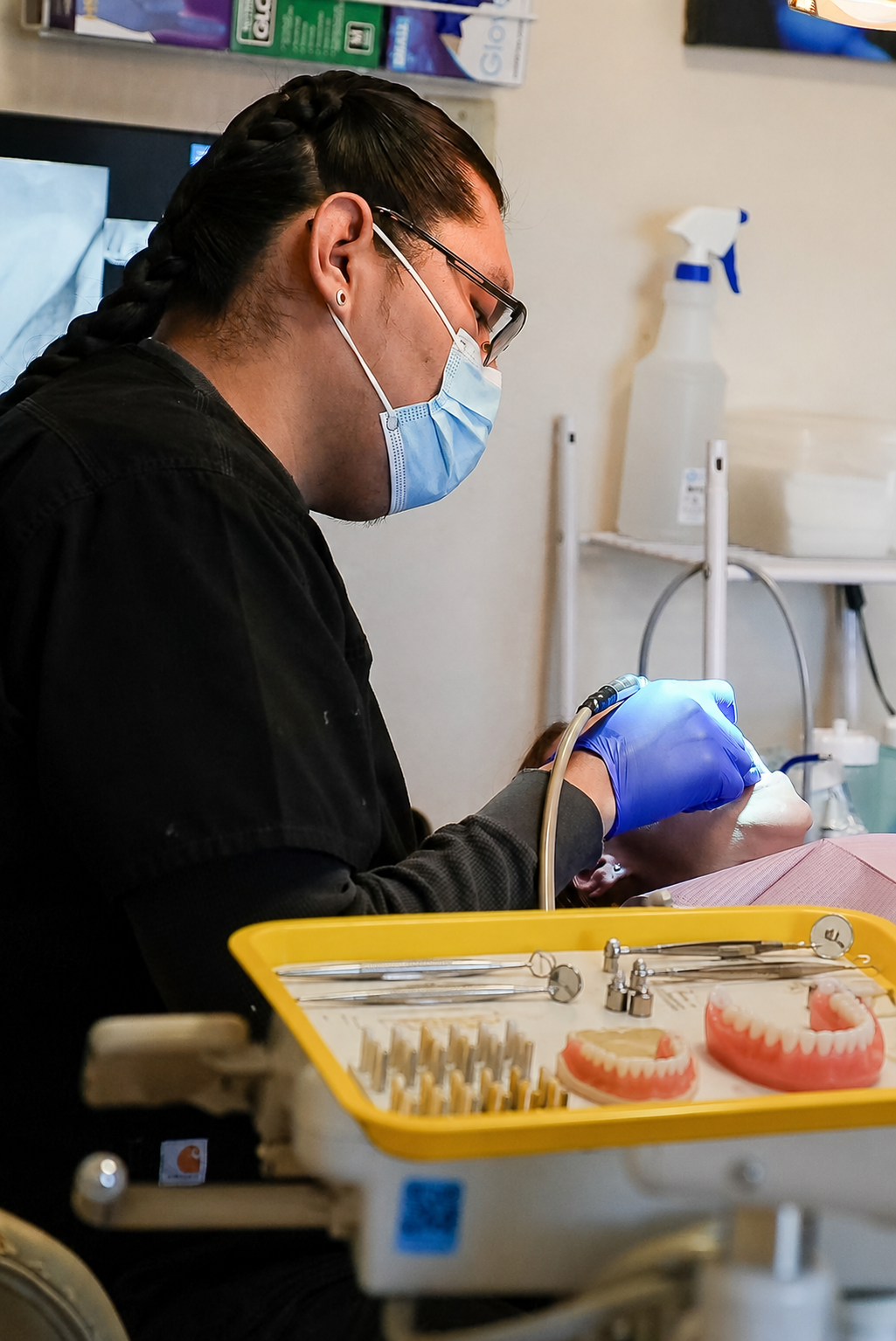 Dentist in blue gloves and mask working on a patient’s teeth beside a tray of tools