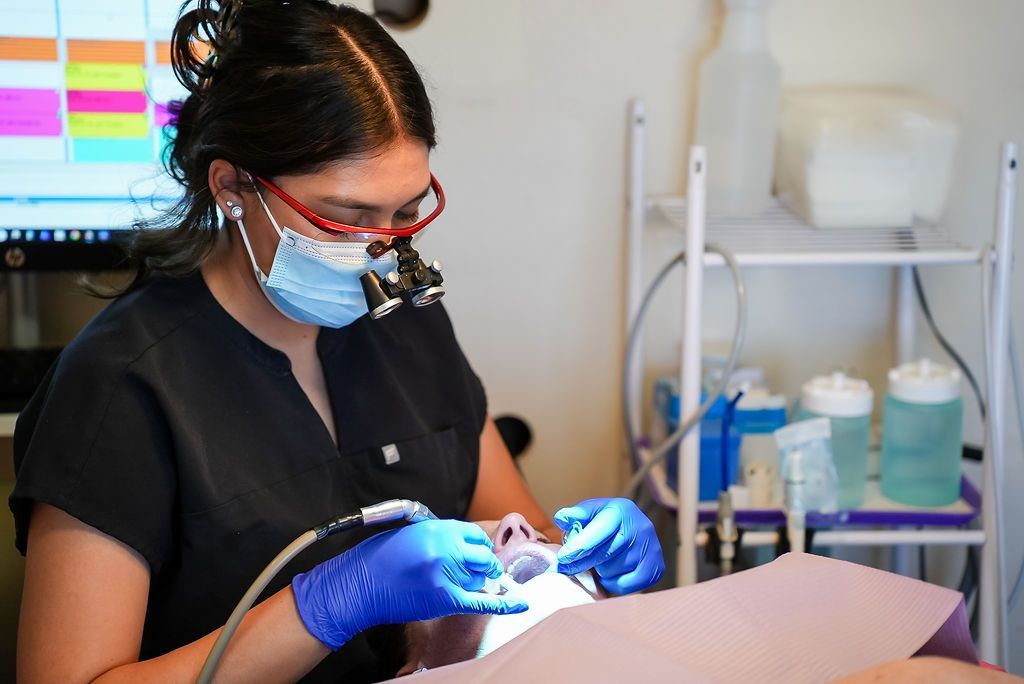 Dentist in black scrubs and blue gloves examining a patient in a dental clinic