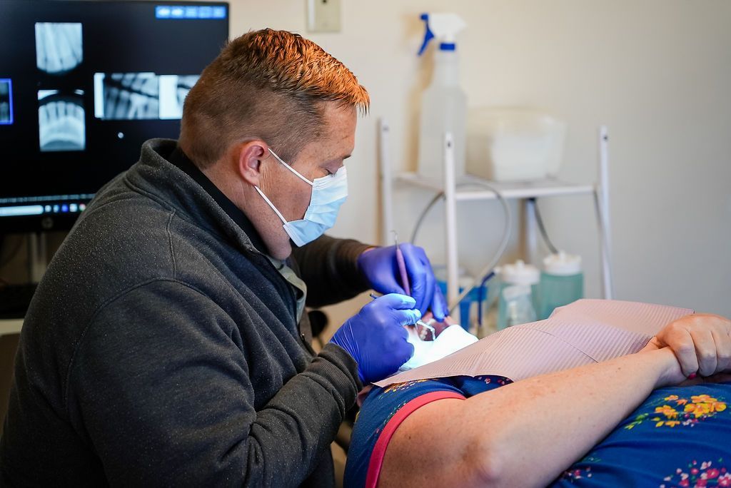 Dentist wearing gloves and mask examines a patient’s mouth in a clinical exam room