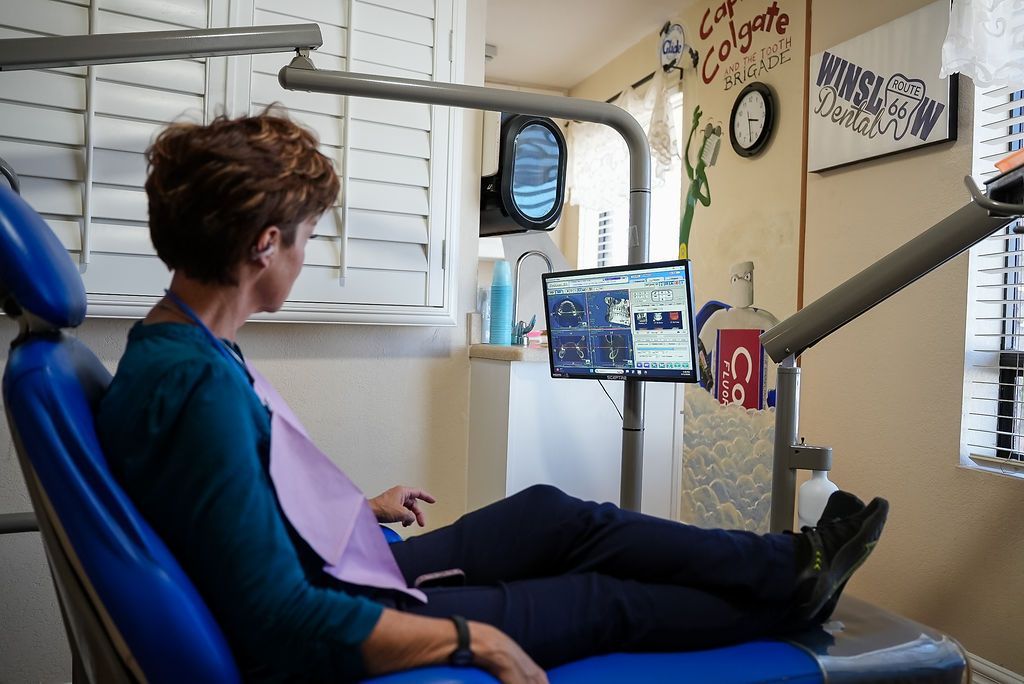 Person reclines in a dental chair while watching a screen in a bright exam room.