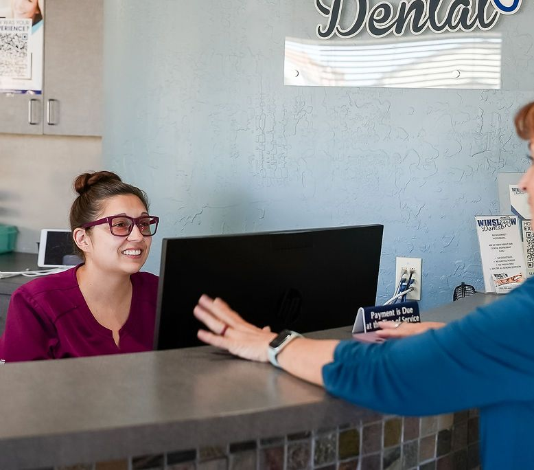 Smiling receptionist behind a counter, talking with a customer in a blue shirt
