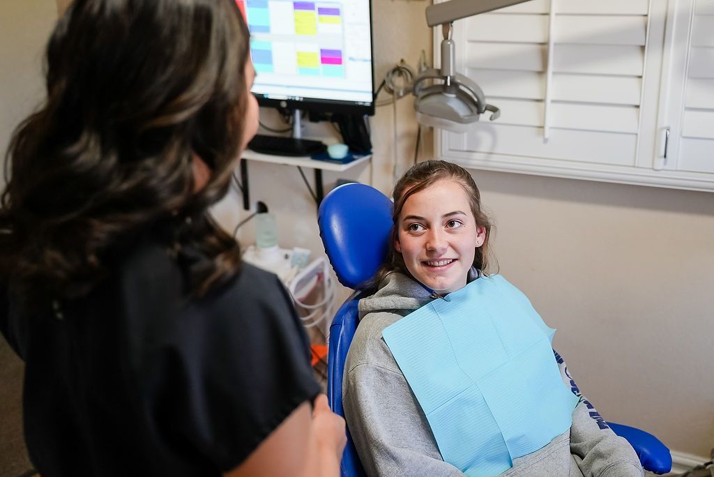 Dentist office visit: smiling patient in blue bib seated in a chair while a clinician stands nearby