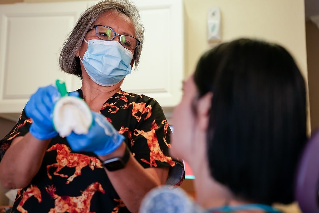 Healthcare worker in mask and gloves speaking to a seated patient in a clinic