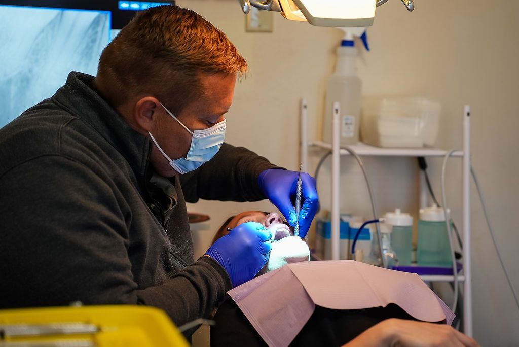 Dentist in mask and gloves treating a patient in a clinic, using a blue dental light.