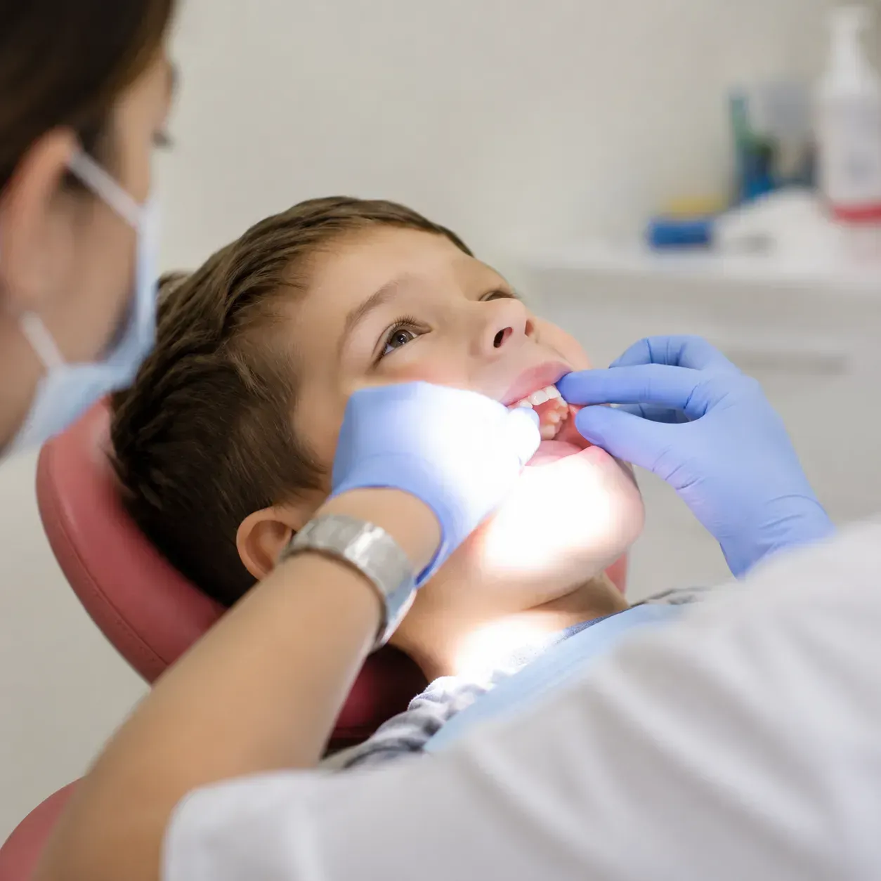 Dentist examining a child’s teeth with gloved hands and a bright exam light