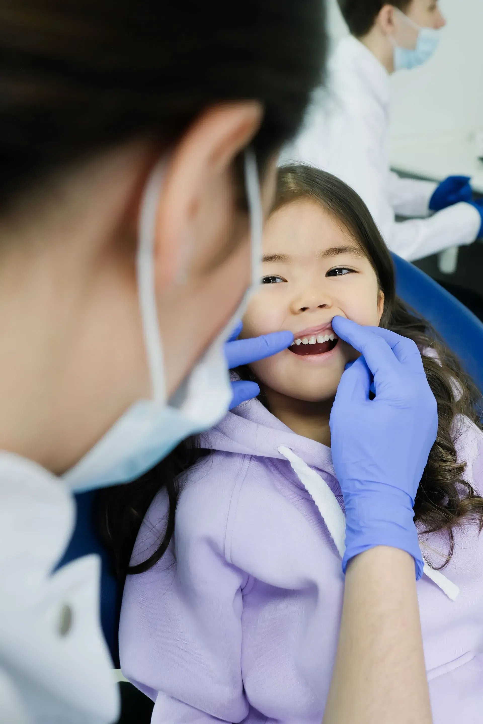 Dentist checking a smiling child’s teeth with gloved hands in a clinic