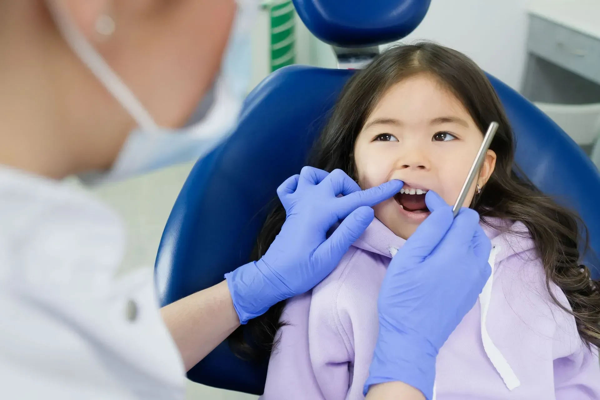 Dentist examining a child’s teeth in a dental chair, with blue gloves and tools visible