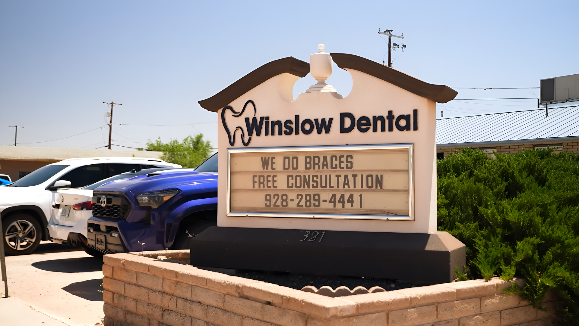 Winslow Dental roadside sign with business name, hours, and phone number by parked cars