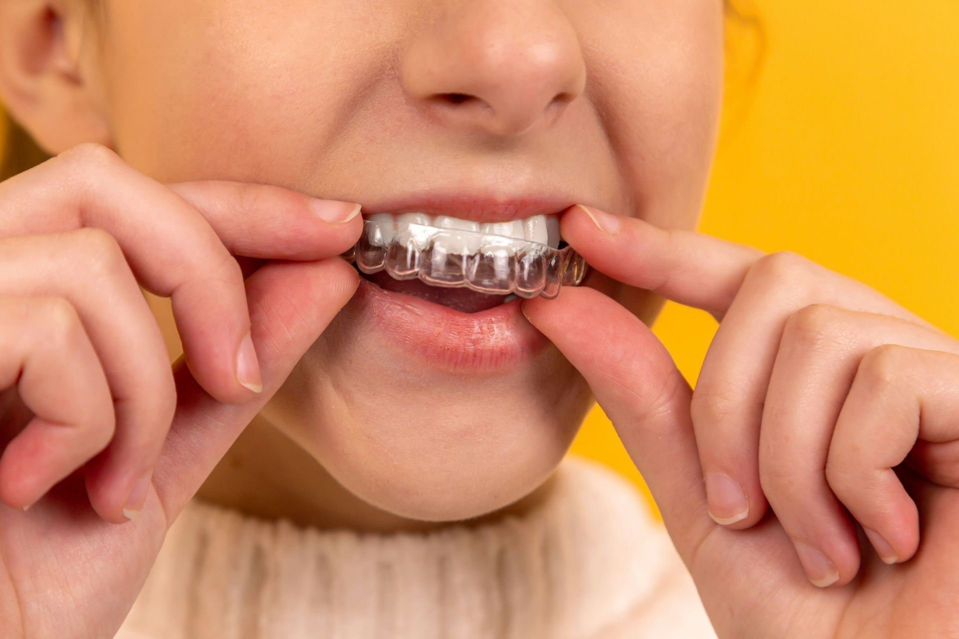 Person adjusting clear braces on teeth against a yellow background