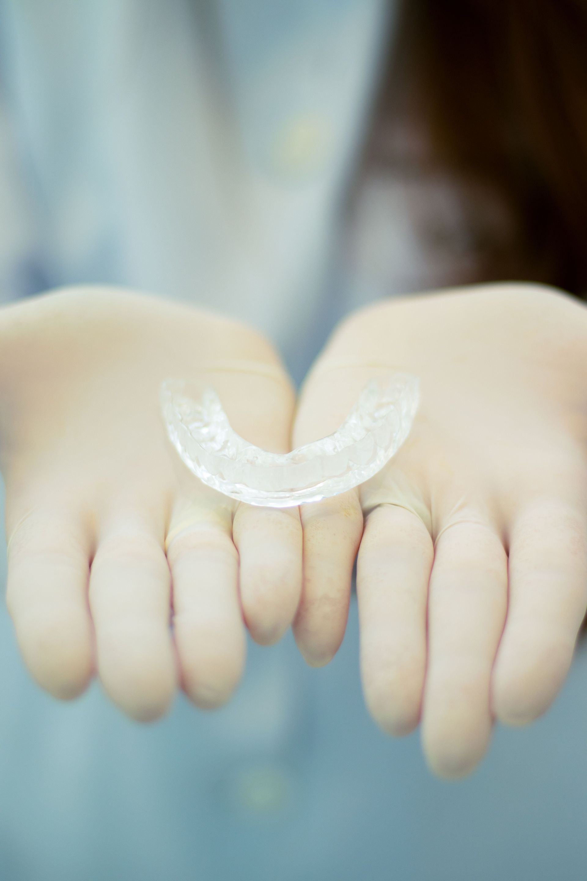Hands holding a clear dental aligner against a blurred background