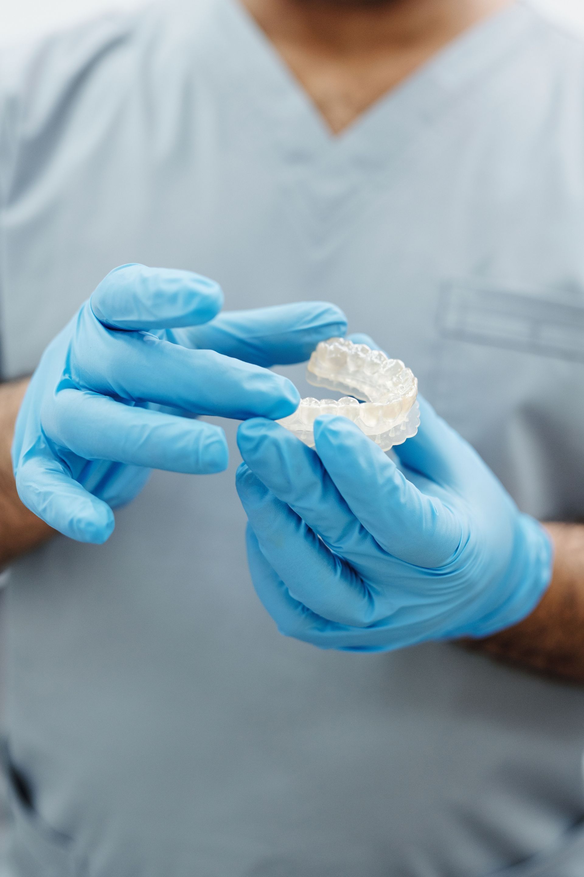Blue-gloved hands holding a clear dental aligner against a white lab coat