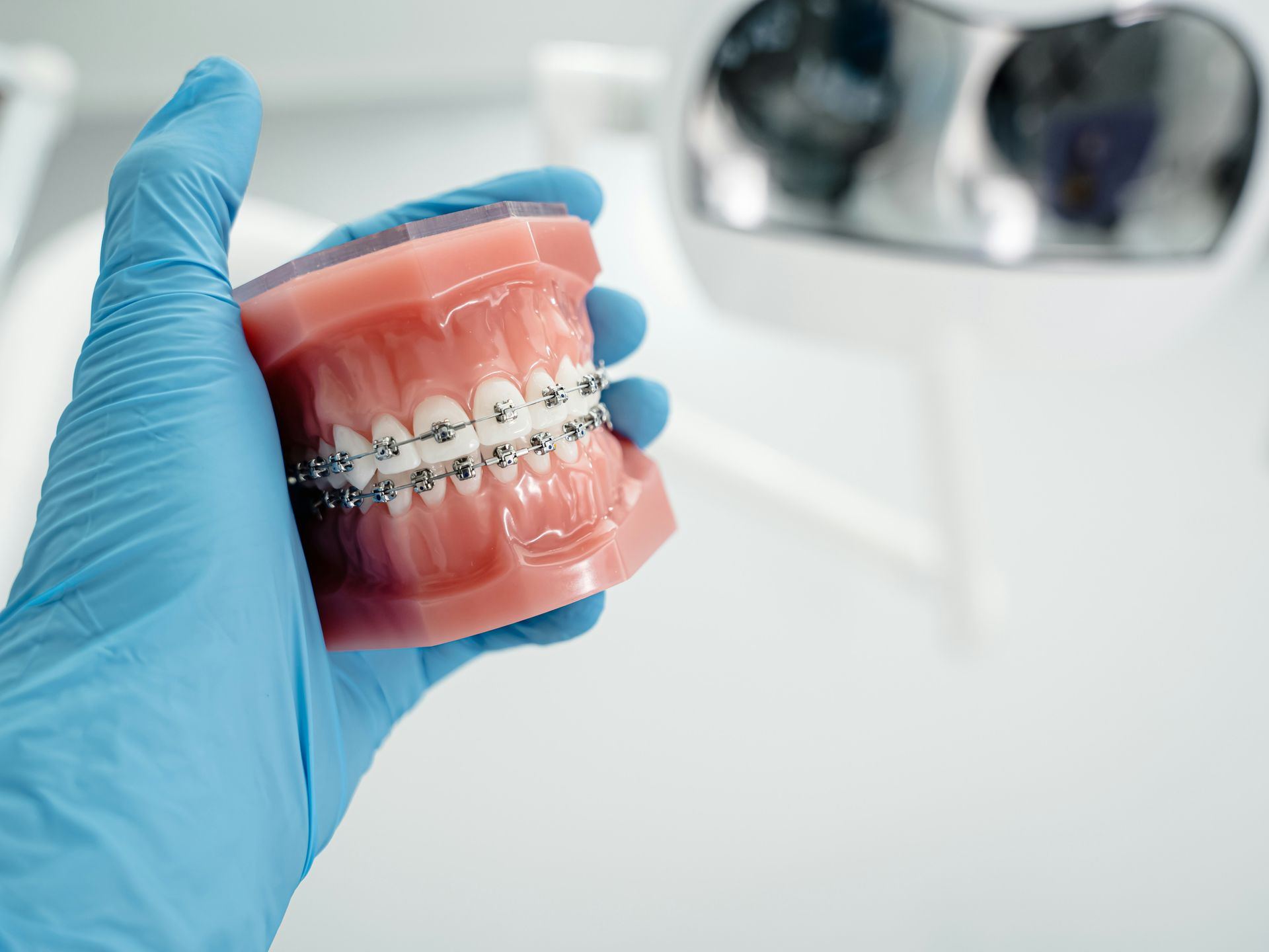 Blue-gloved hand holding a clear dental aligner with metal braces against a white clinic sink background