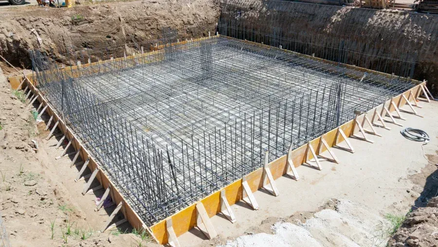 Foundation rebar grid in a dug-out construction pit with yellow forms along the edge