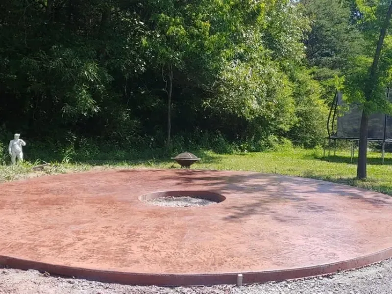 Large circular brick platform with a central fire pit in a grassy park, surrounded by trees