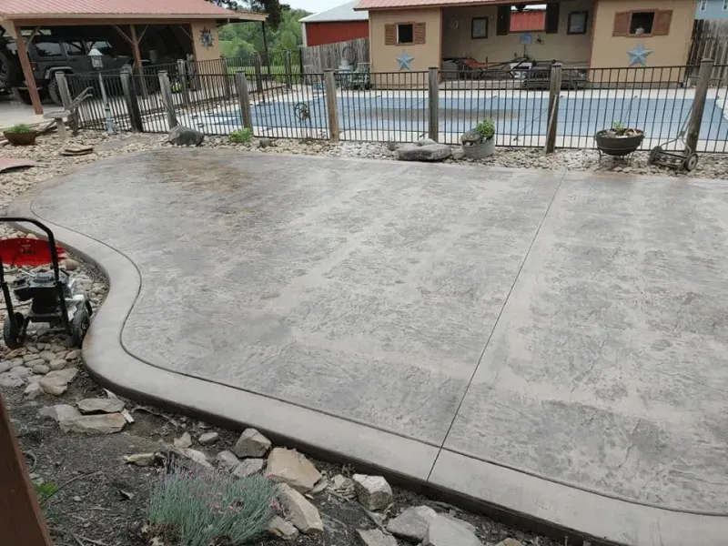 Freshly poured concrete driveway beside a gravel yard and metal fence in front of houses