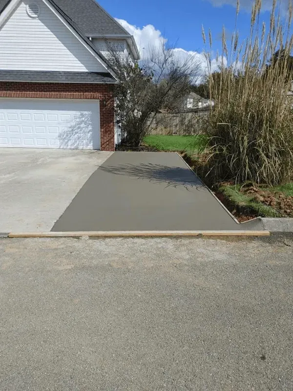 New concrete driveway ramp beside a garage, sloping up from the street.
