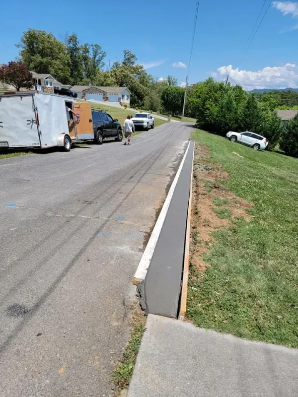 Road with parked trucks and cars beside a grassy slope under a blue sky