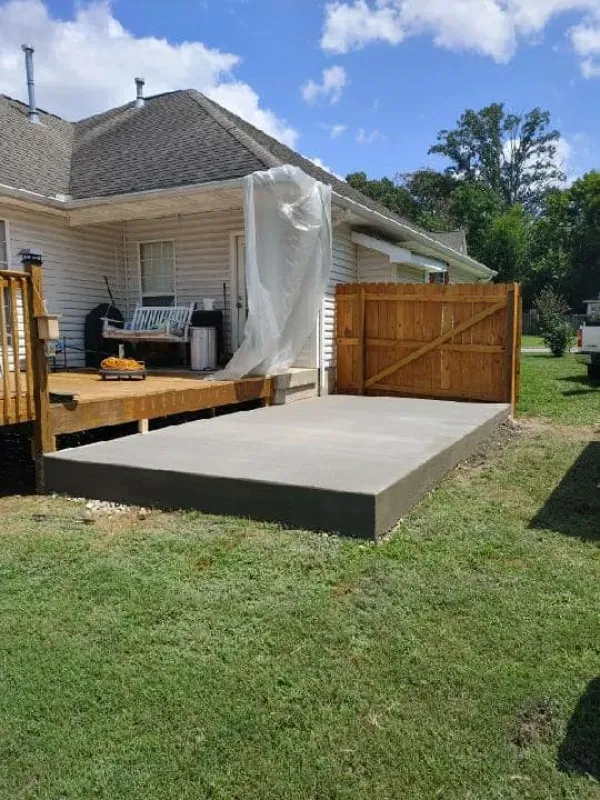 Backyard deck with a concrete ramp and wooden gate beside a house, with a tarp covering the porch.