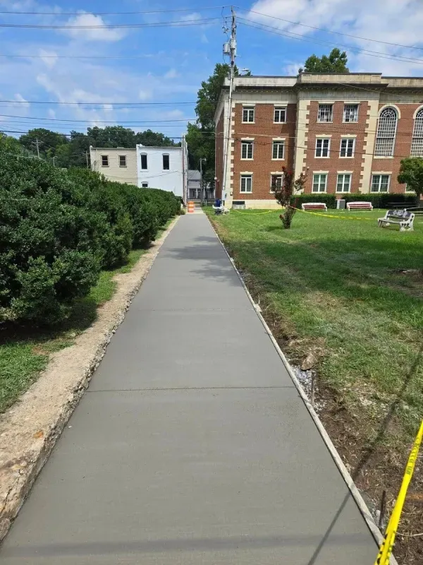 Sidewalk leading past bushes to a brick building and grassy lawn under a blue sky.
