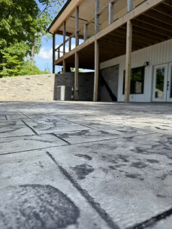 Outdoor patio with stamped concrete, stone wall, and a covered building entrance with glass doors