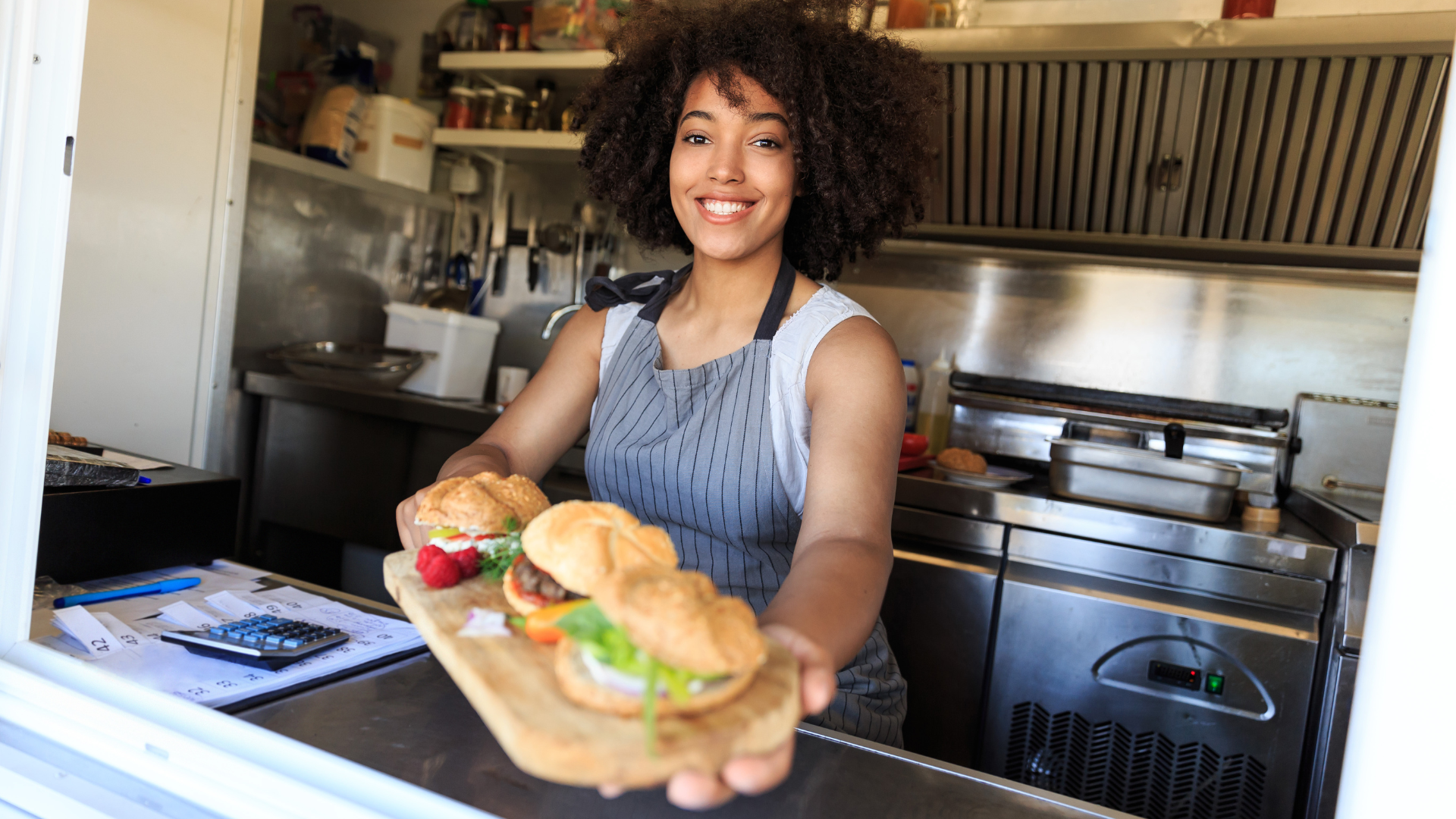 A woman is holding a sandwich in front of a window at a food truck.