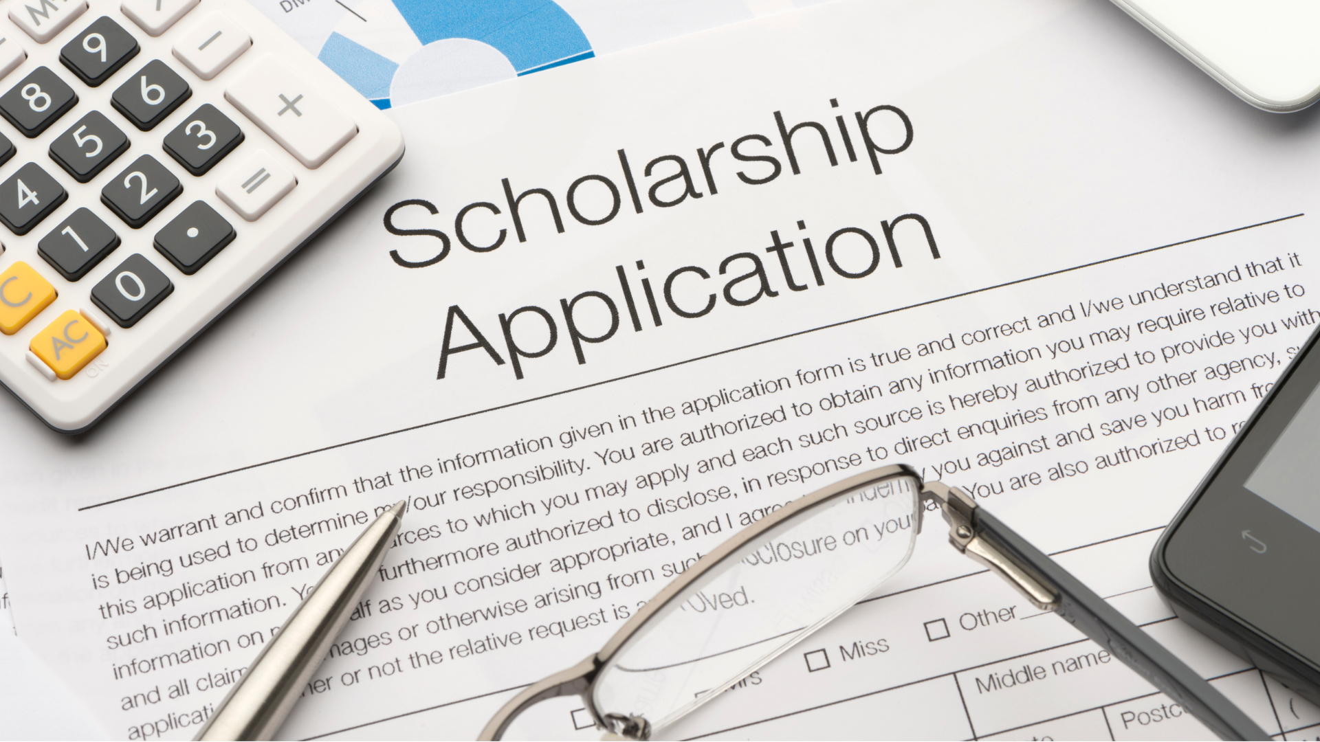 A calculator , glasses , a pen and a tablet are on top of a scholarship application.