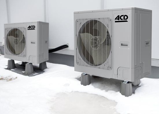 Deux unités de climatisation sur des plateformes grises posées sur une surface plane et blanche, avec un tuyau noir entre elles.