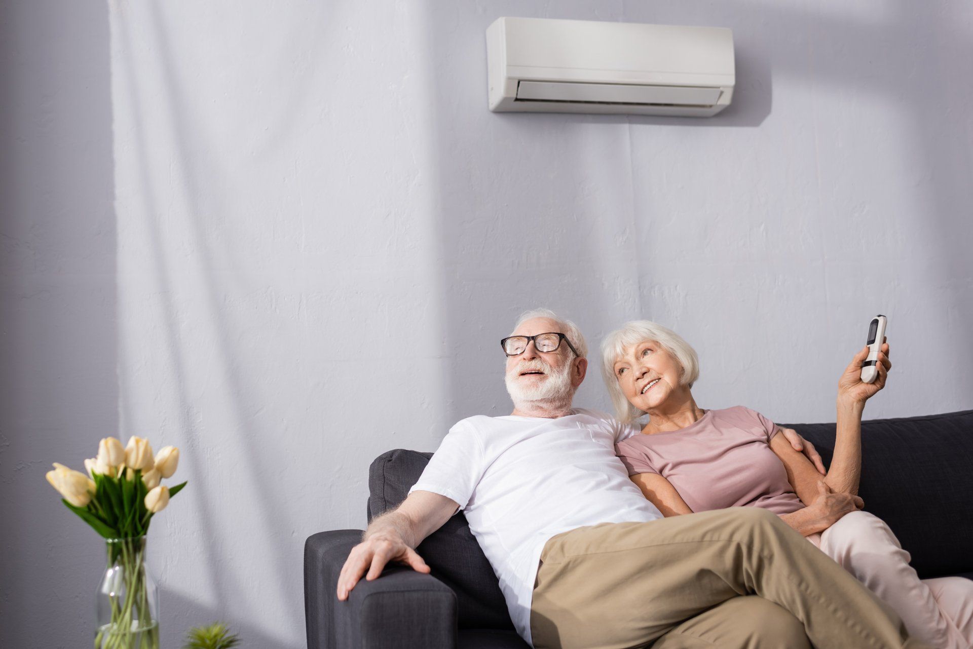 Un couple sur un canapé sous un climatiseur, la femme tenant une télécommande, regardant vers le haut.