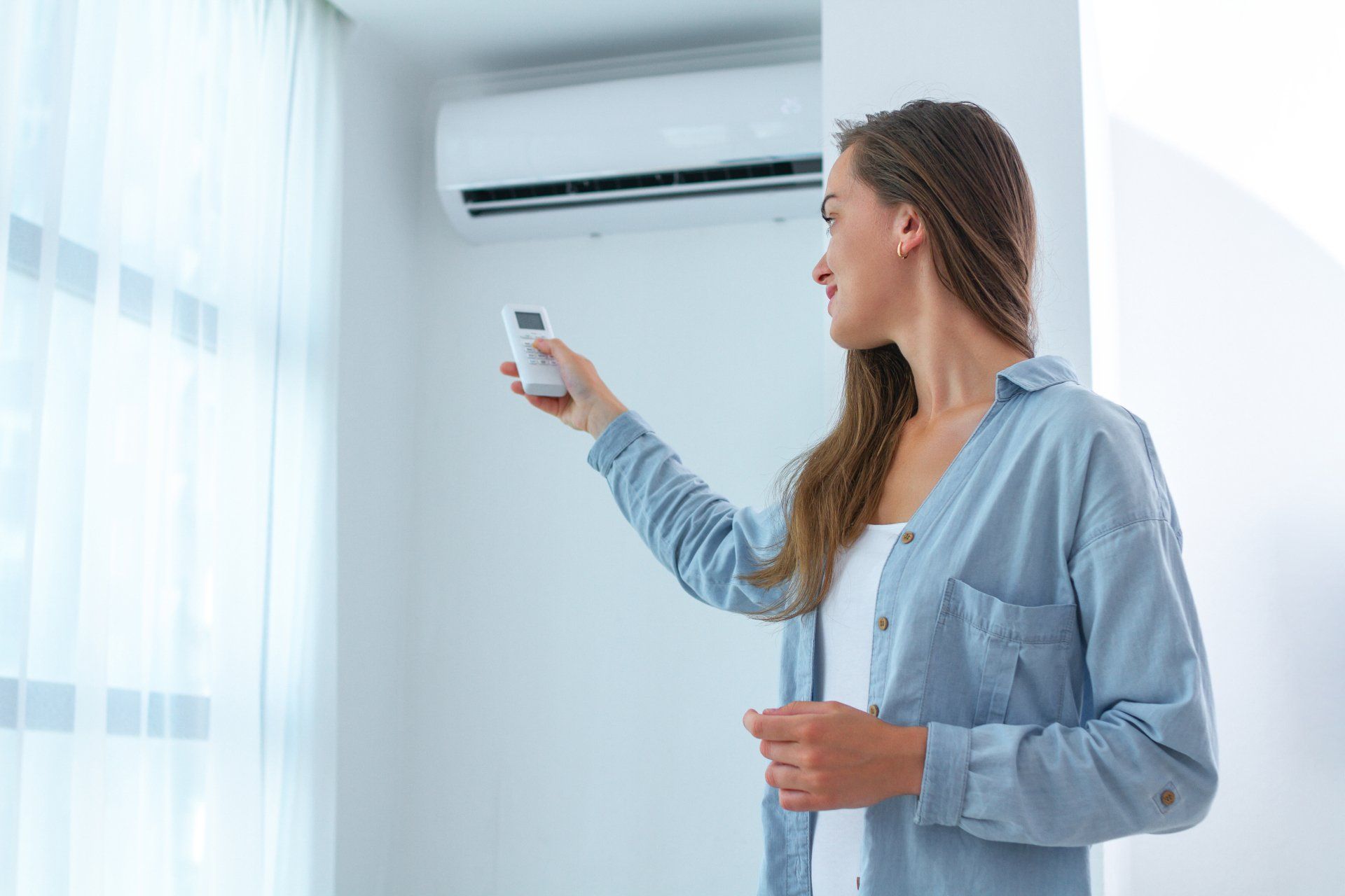 Woman using a remote to adjust a wall-mounted air conditioner in a bright room