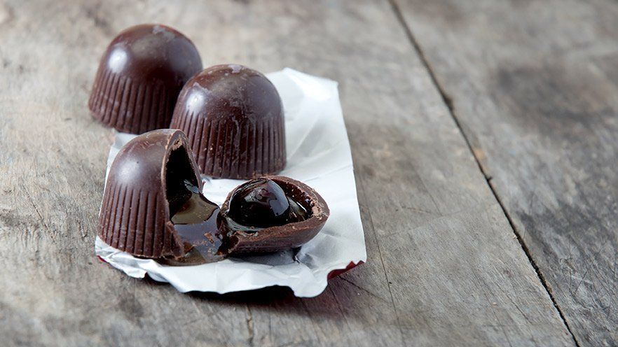 Three chocolates are sitting on a piece of paper on a wooden table.