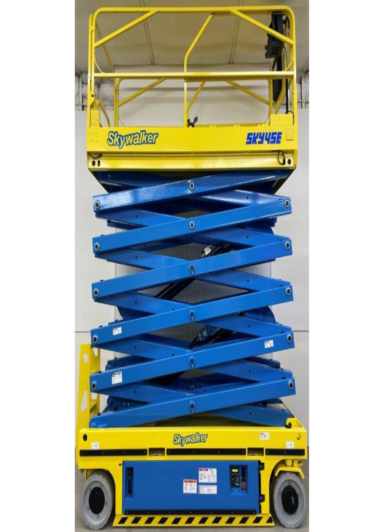 A blue and yellow scissor lift is sitting in front of a wall.