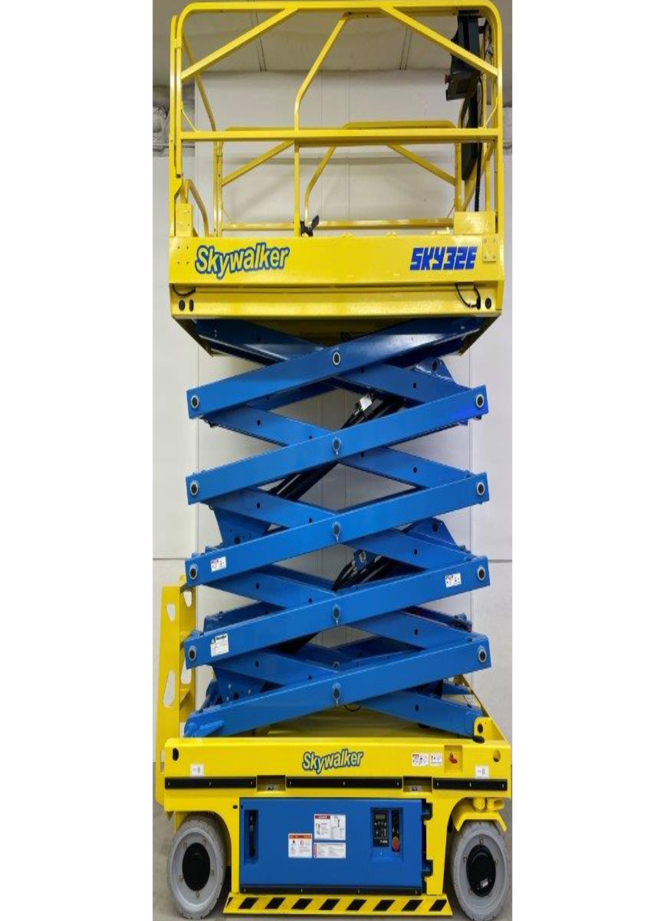 A blue and yellow scissor lift is sitting in front of a white wall.