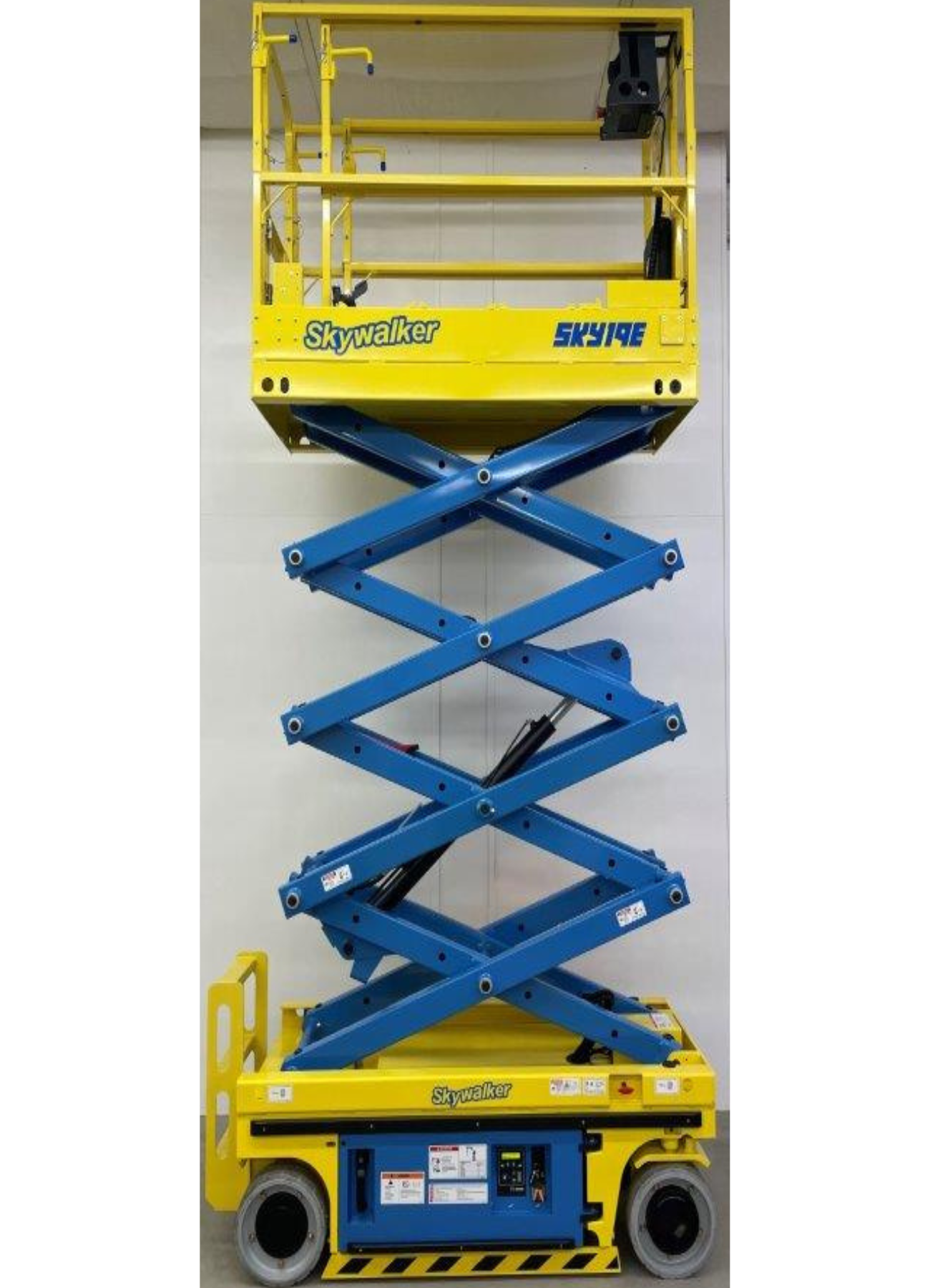 A yellow and blue scissor lift is sitting in front of a white wall.