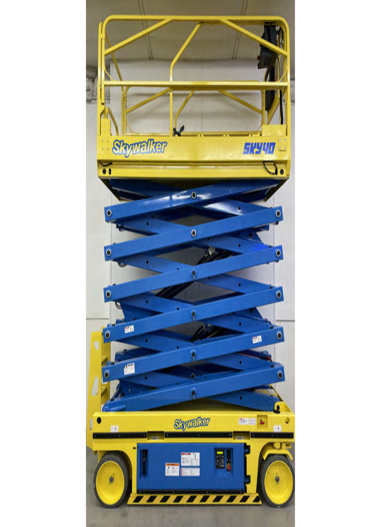 A blue and yellow scissor lift is sitting in front of a wall.