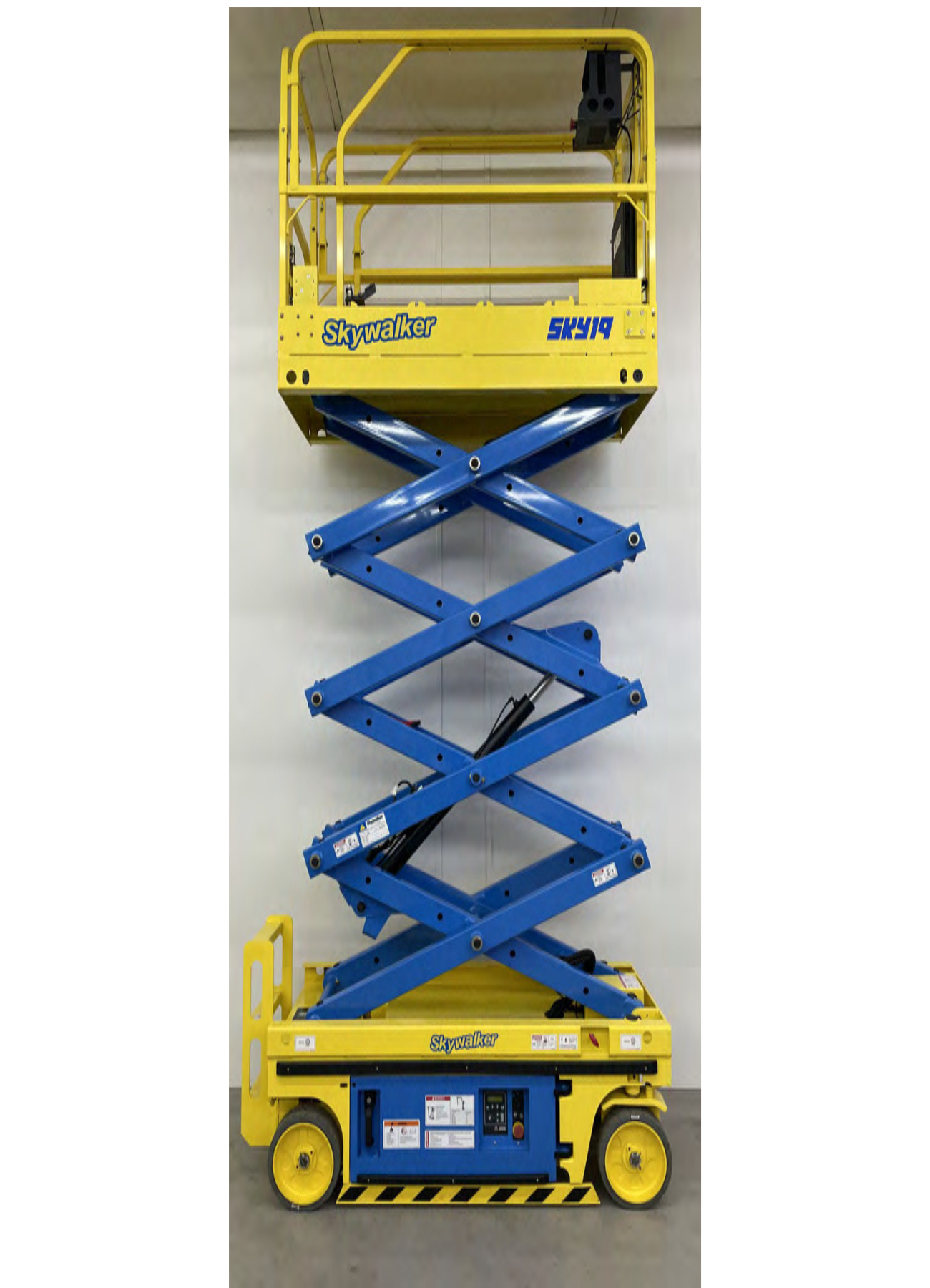 A blue and yellow scissor lift is sitting in front of a white wall.