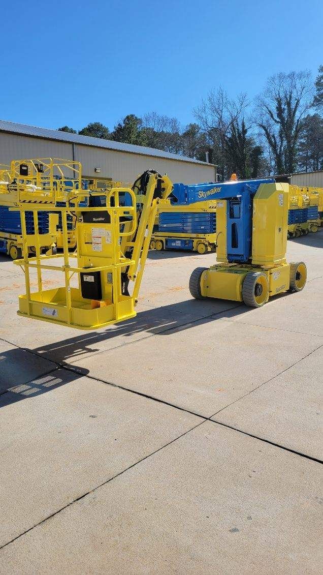 Yellow and blue articulated boom lift on a concrete surface under a blue sky.