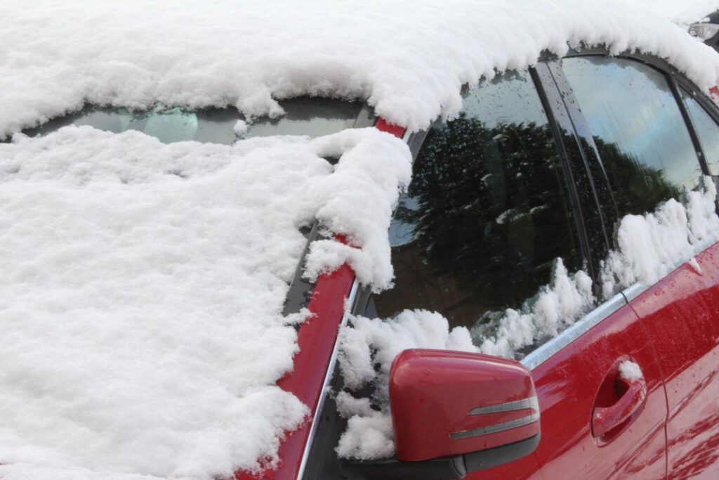 Red car windshield and side mirror covered in thick snow and ice