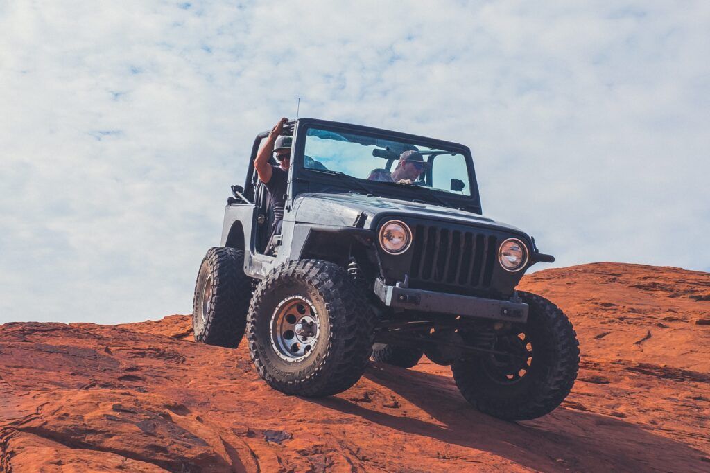 Black Jeep Wrangler driving over a red rocky hill under a cloudy sky