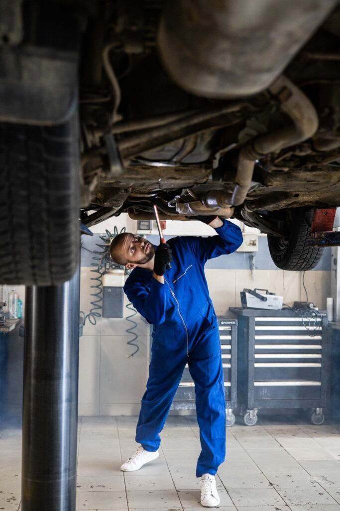 Mechanic in blue coveralls working under a raised car in an auto repair shop