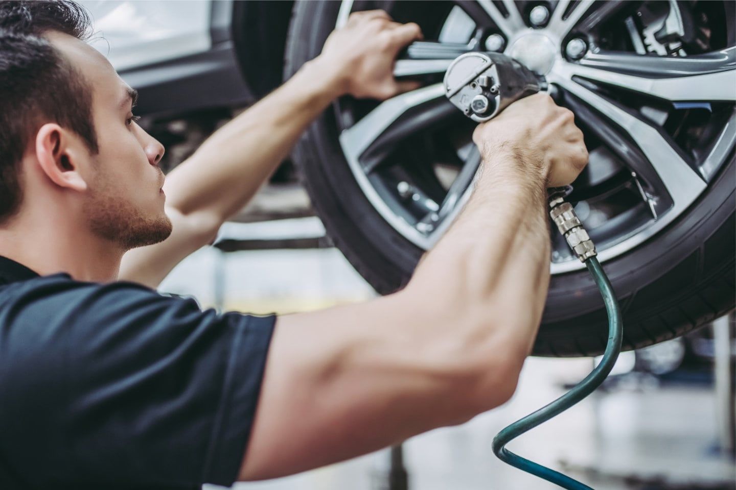 Mechanic tightening lug nuts on a car wheel with a pneumatic wrench in a garage