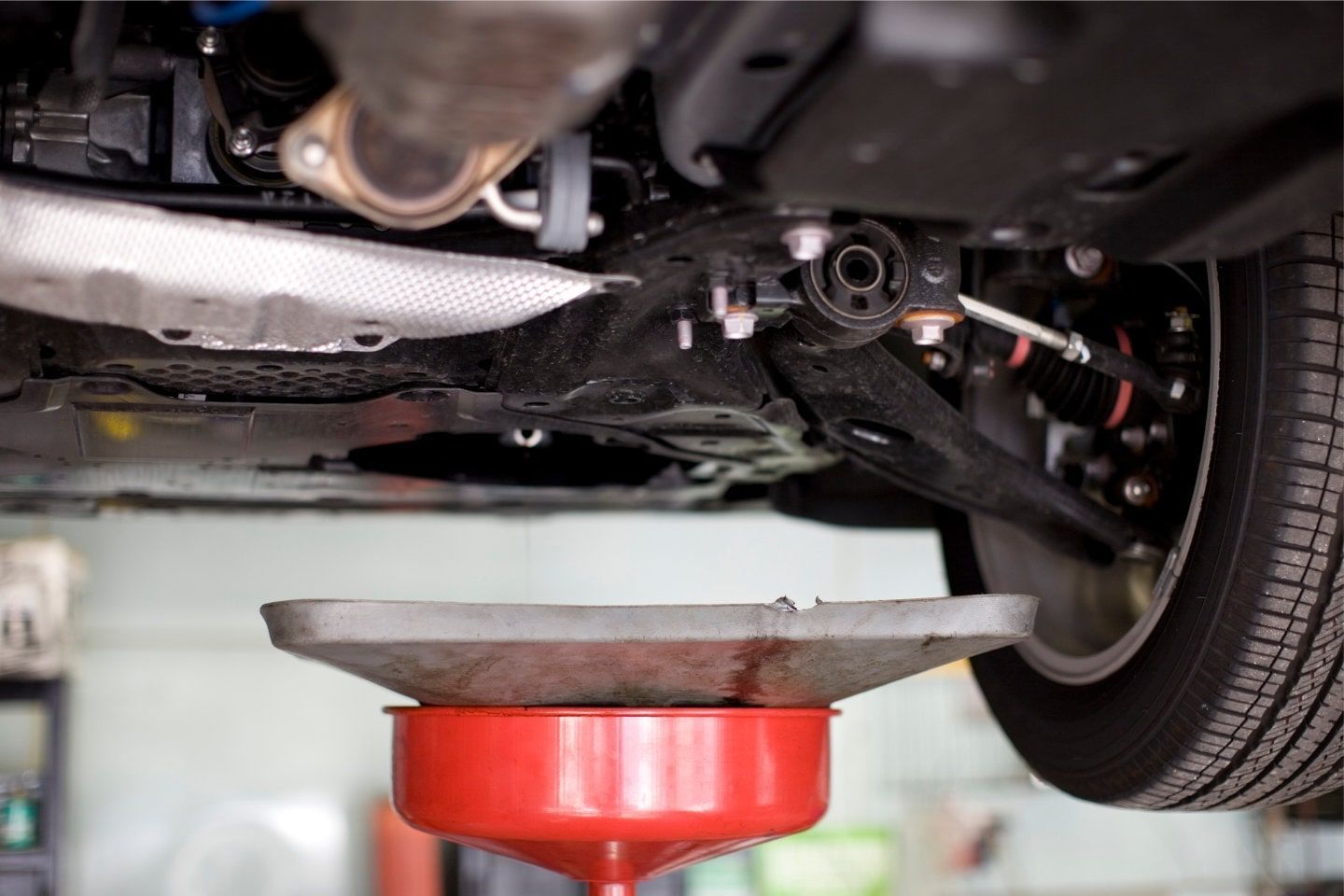 Car underside lifted on a red jack stand in a garage, with a tire visible on the right.