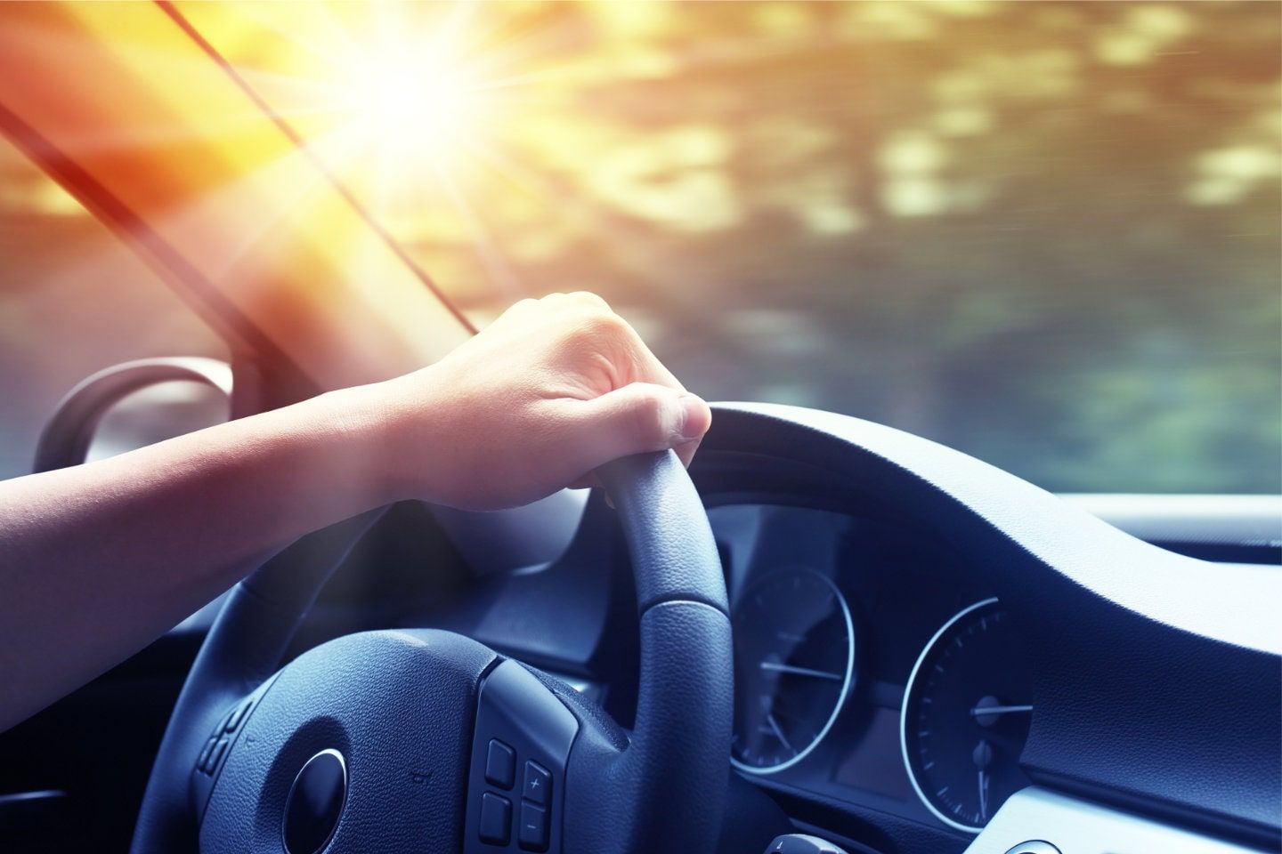 Driver’s hand on steering wheel in car interior with warm sunlight through windshield