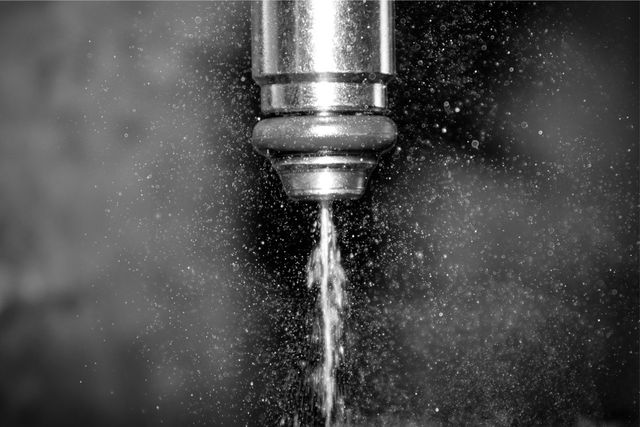 Close-up of a metal drill bit cutting through material, with water spraying around it.
