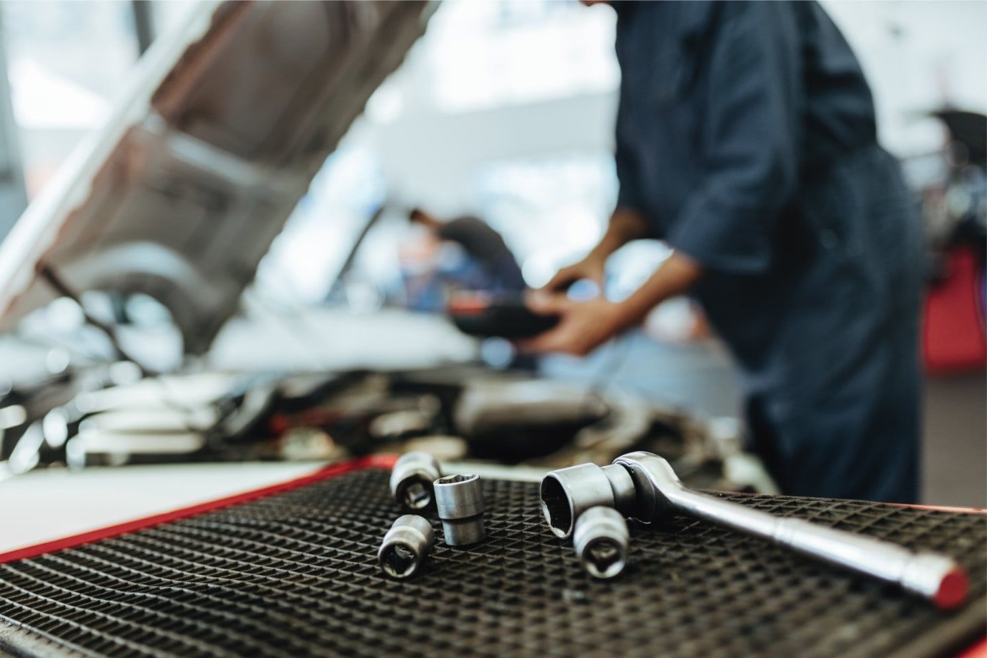 Mechanic’s tools on a workbench in a garage, with a blurred technician in the background