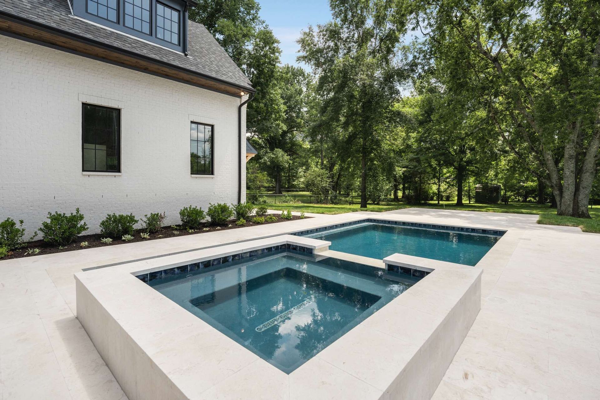 A modern pool area with a spa and rectangular pool in front of a white brick building.