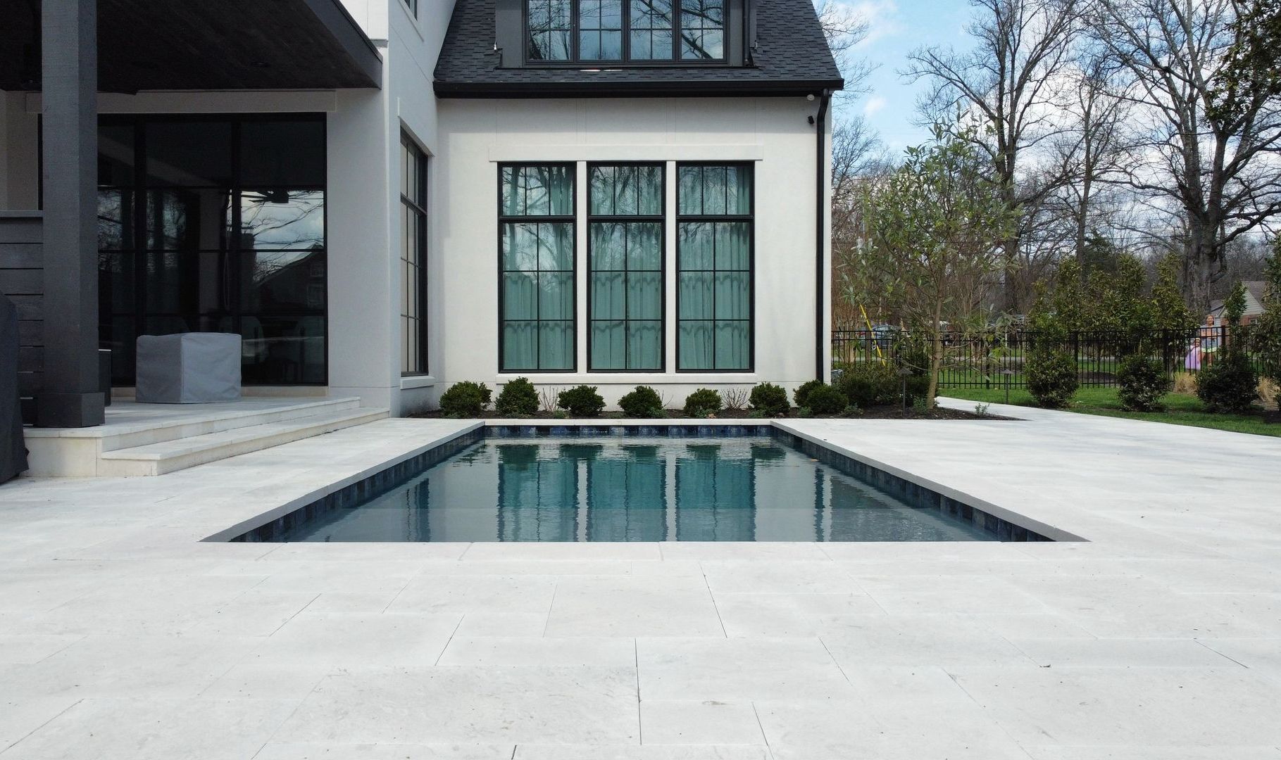 Rectangular pool in front of a white house with black-framed windows. Blue water reflects sky.
