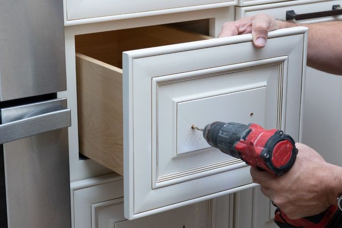 Person using a red drill to install a white cabinet drawer front in a kitchen.