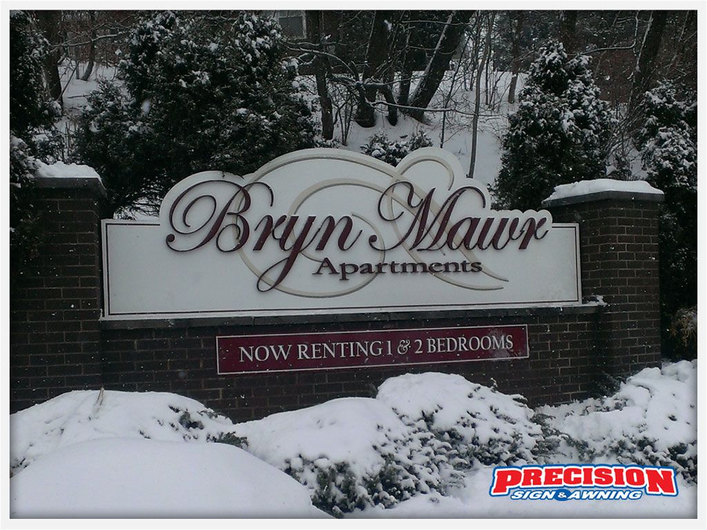Sign for Bryn Mawr Apartments in winter, with snow and brick pillars;